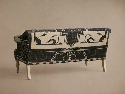 Close-up of Anya Settee's curved armrest and seat in distressed black and cream geometric abstract patterned upholstery, wood leg.