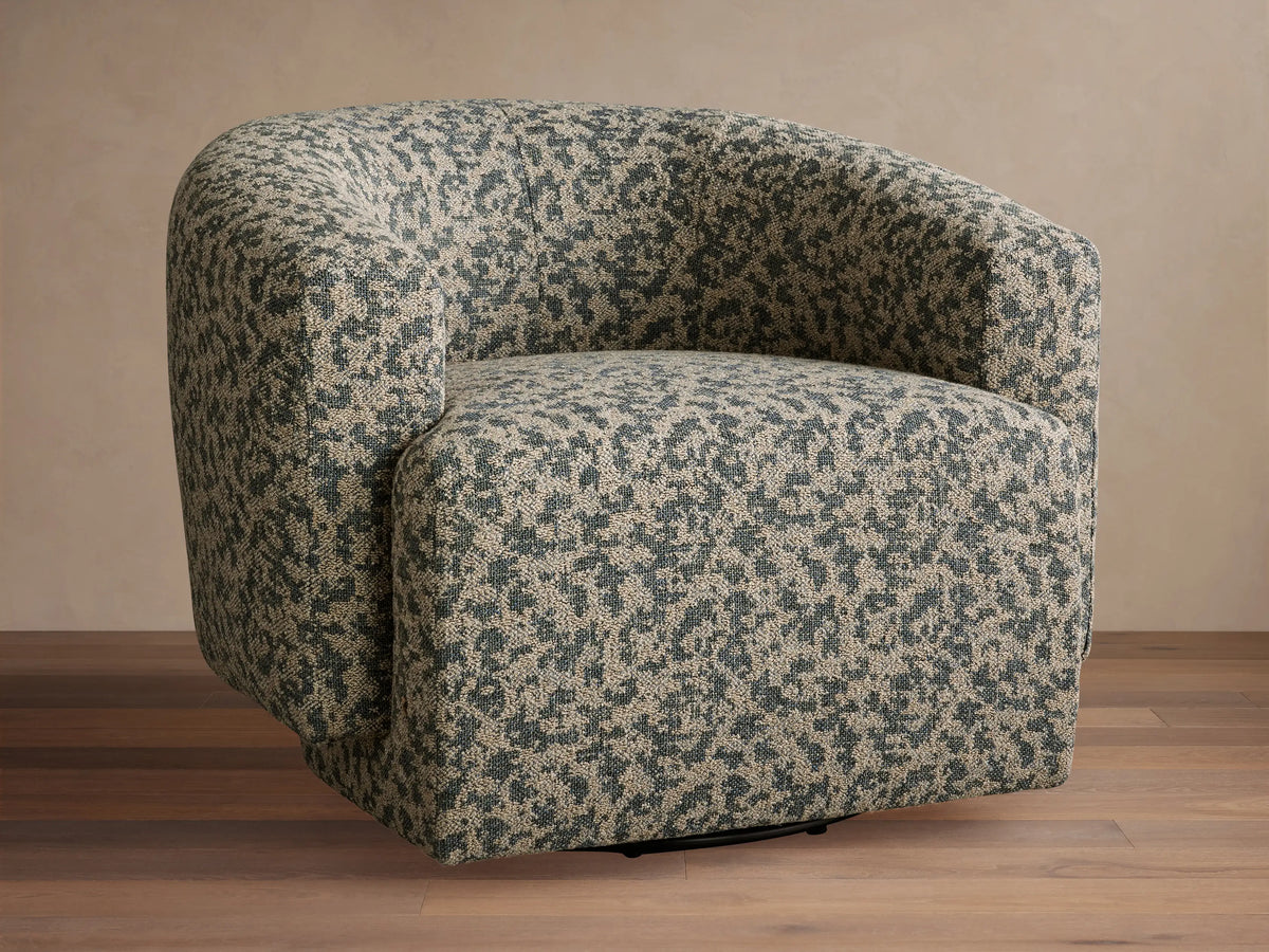 Hamlin Swivel Chair with a rounded bucket shape, upholstered in a dappled dark green and light tan fabric, on a wooden floor.
