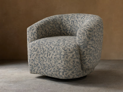 Hamlin Swivel Chair with a rounded bucket shape, upholstered in a dappled dark green and light tan fabric, on a wooden floor.