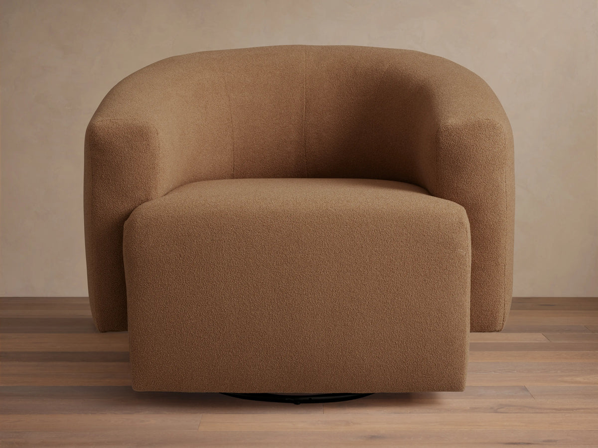 Two gold Hamlin Swivel Chairs with plush, curved backs flank a small gold side table in a sunlit living room.