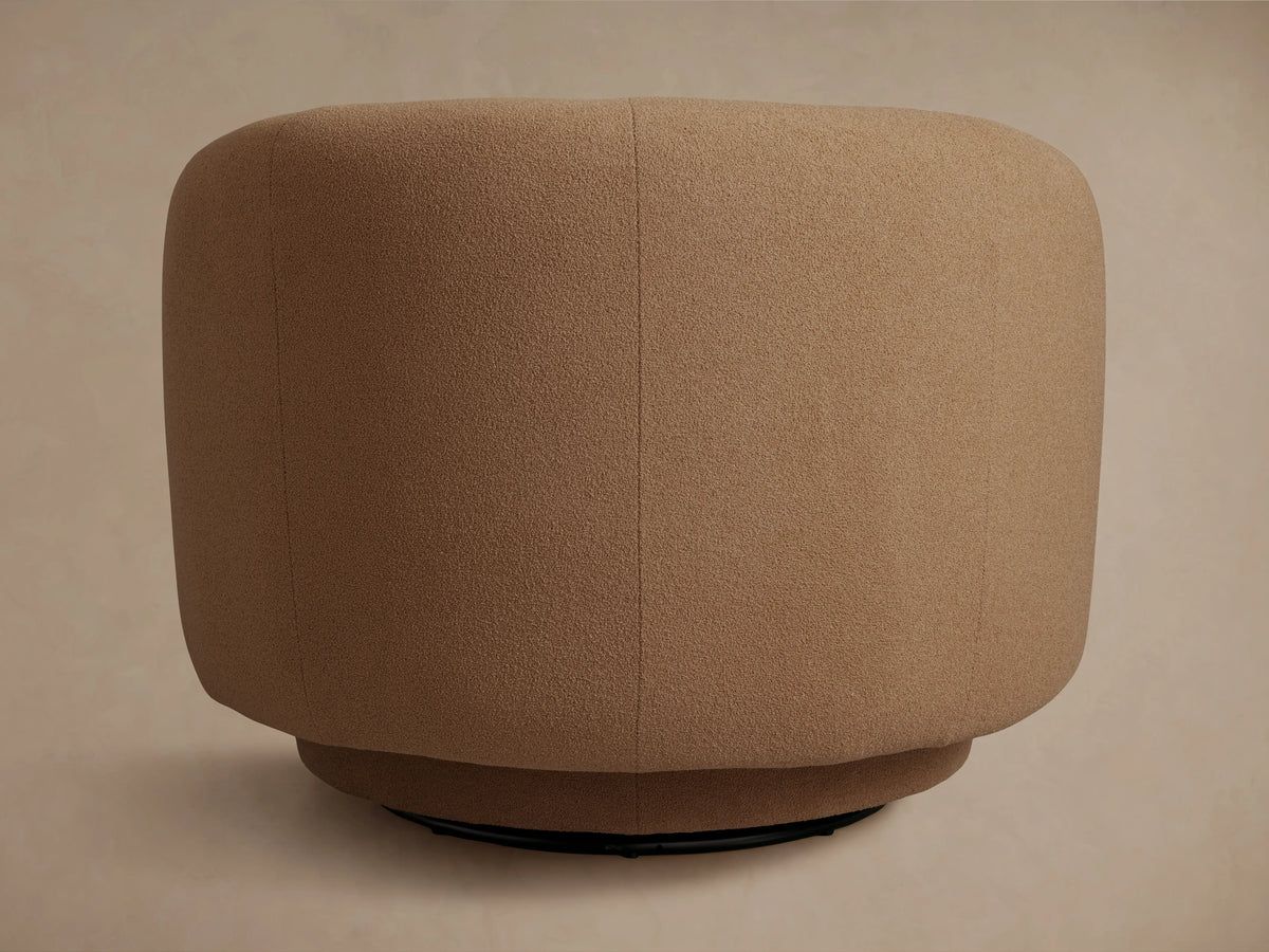 Side view of a modern, rounded camel-colored textured swivel armchair. Features wide, low-profile arms on a dark base.