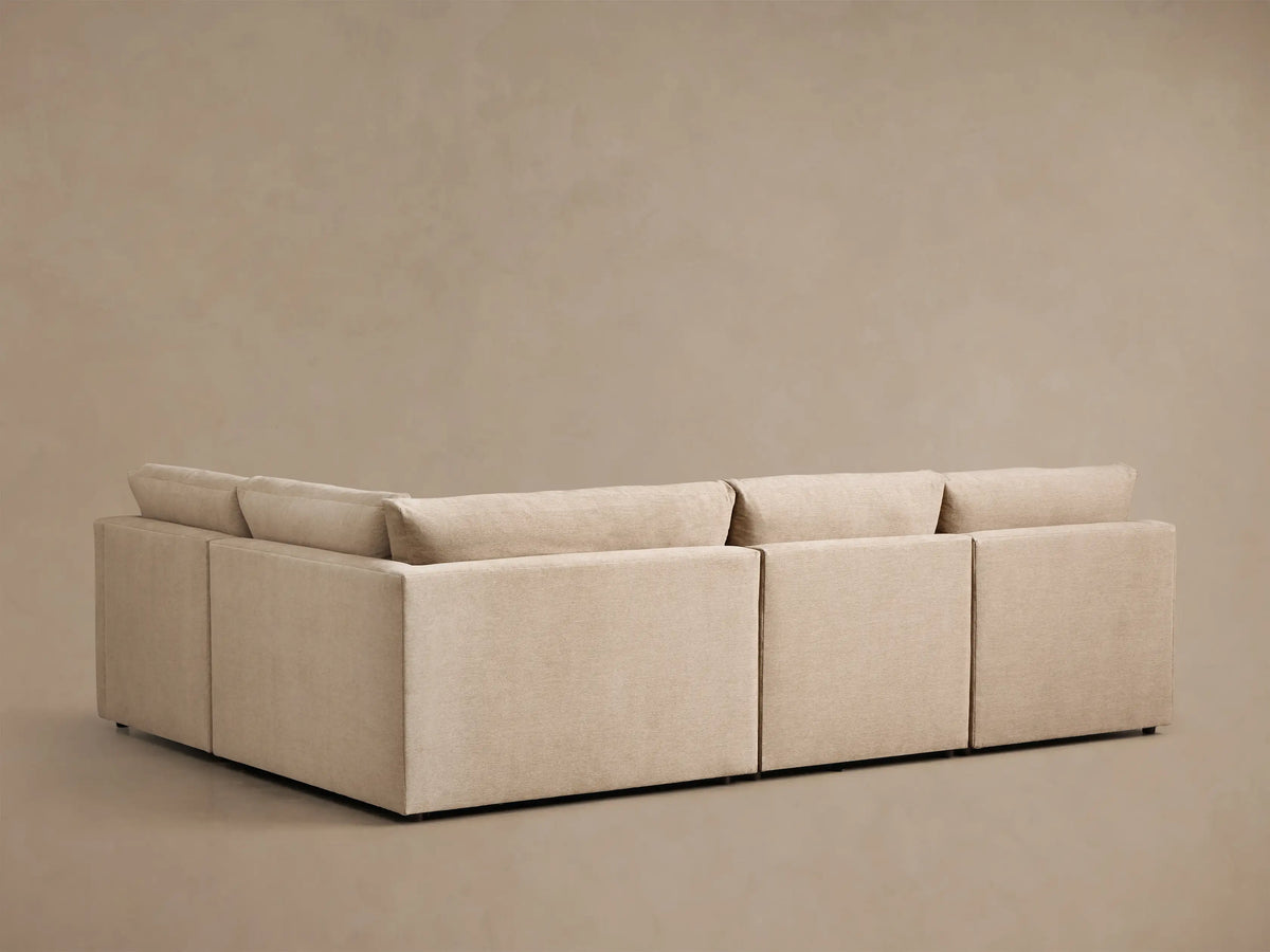 Rear view of the beige Kipton Slope Arm Four-Piece Motion Sectional, showing its four solid sections and back cushions.