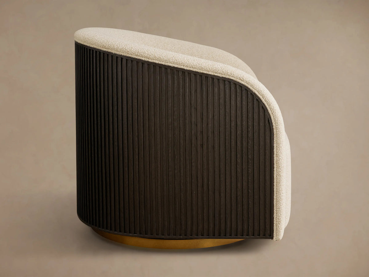 Side profile of a Finnley Swivel Chair with cream bouclv© fabric, dark ebony ribbed wood back, and a golden swivel base.