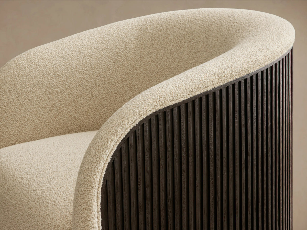 Close-up of the curved back and armrest of the Finnley Swivel Chair, featuring cream textured upholstery and a dark slatted wood exterior.