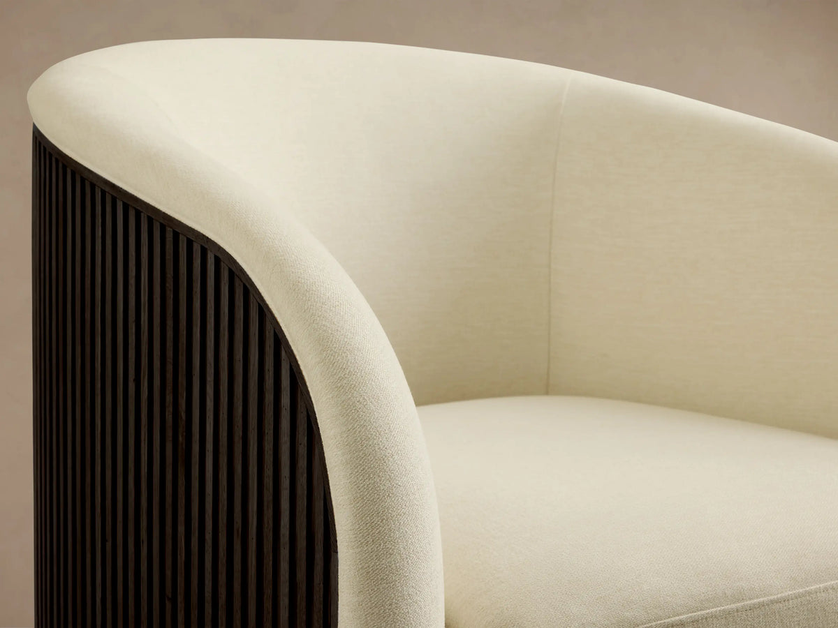 Finnley Swivel Chair in cream fabric, featuring a rounded backrest and plush seat on a wooden floor, with a golden swivel base.