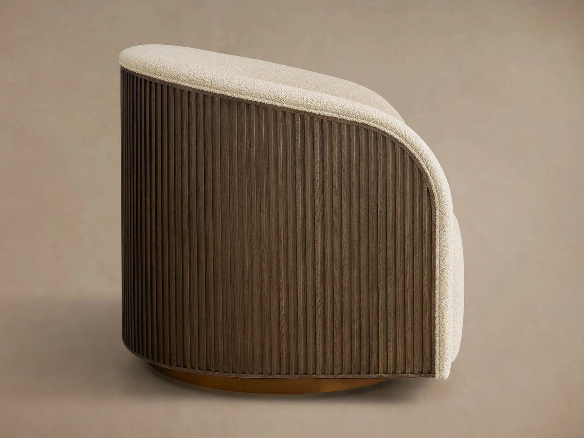 Side profile of the Finnley Swivel Chair, featuring cream textured upholstery and a dark brown fluted wood base on a bronze swivel.
