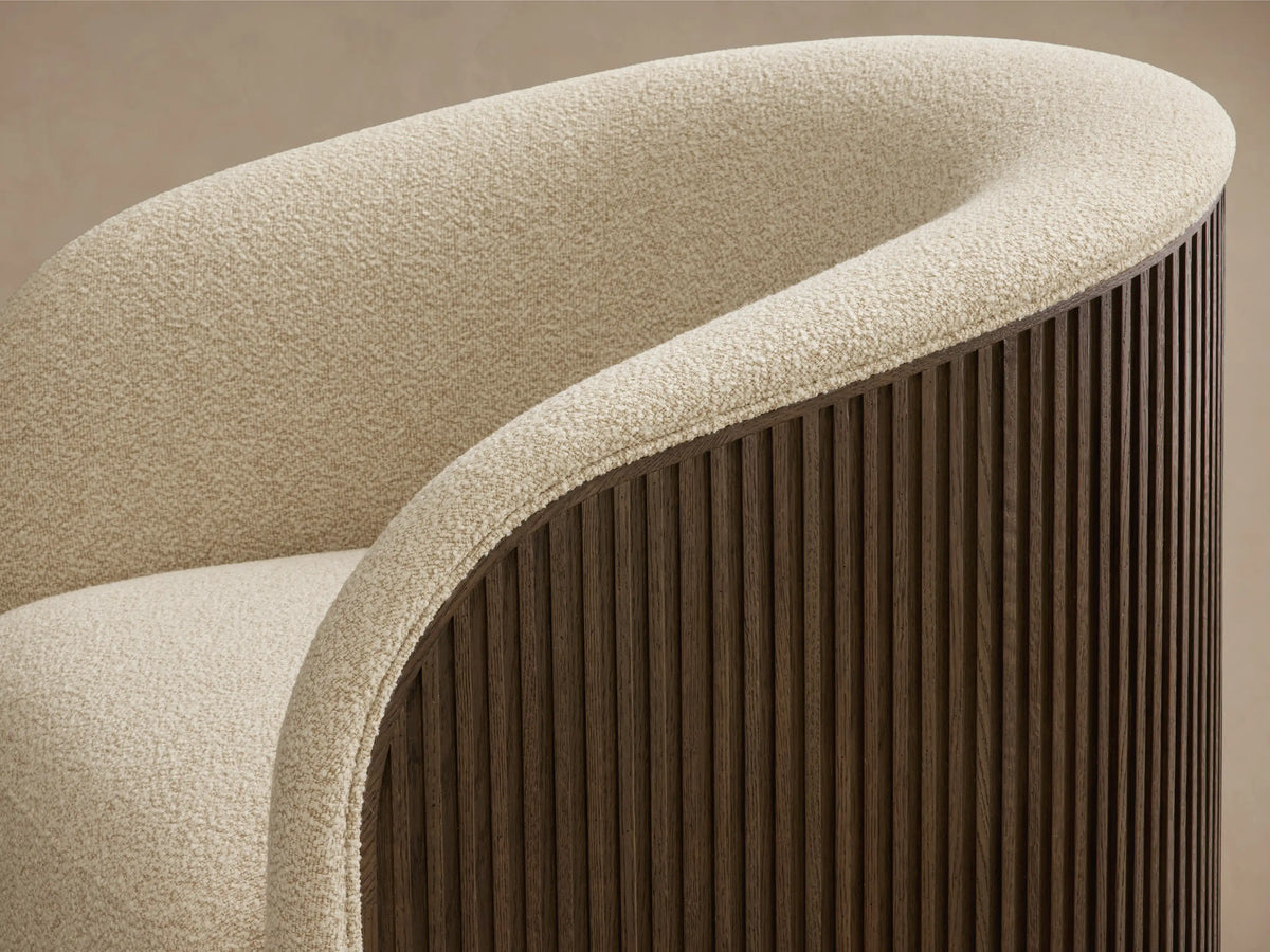 Detail of the curved back and armrest of the Finnley Swivel Chair, featuring cream textured upholstery and a dark wood slatted exterior.