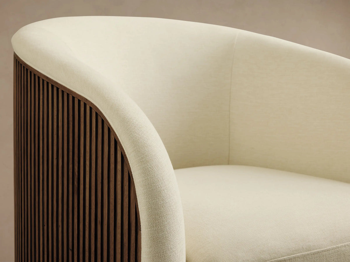 Finnley Swivel Chair in cream fabric, with rounded backrest and seat, on a wooden floor, featuring a gold-toned swivel base.