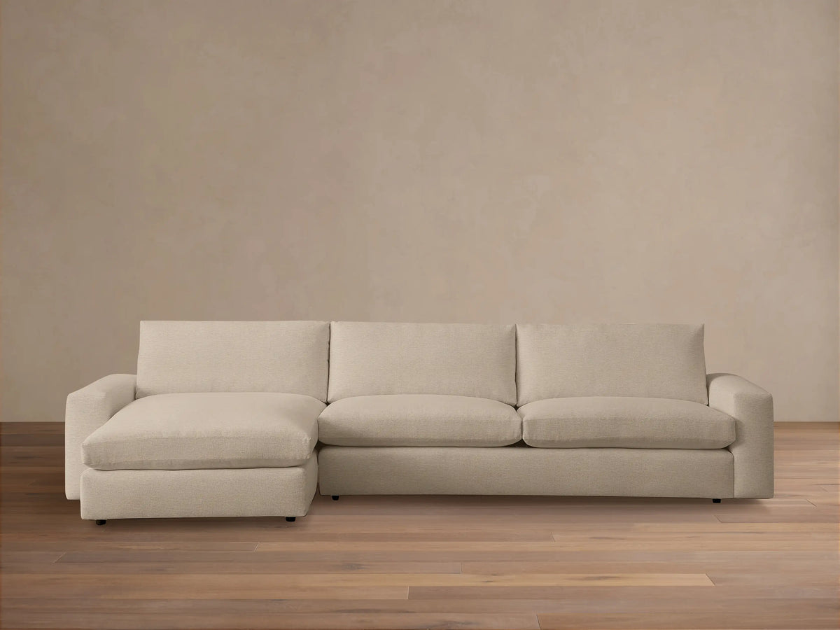 Kipton Wide Arm Two-Piece Chaise Sectional in a beige fabric. It features wide arms, a chaise on the left, and plush cushions on a wooden floor.