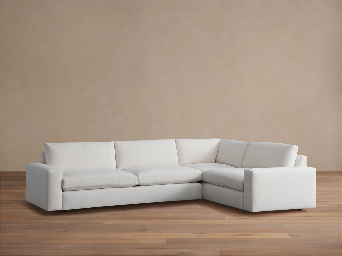 Kipton Wide Arm Two-Piece Sectional in light beige fabric, featuring wide armrests and plush cushions, set on wooden floor.
