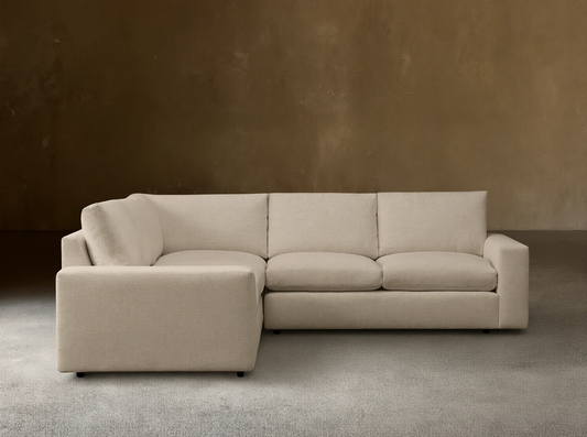 Kipton Wide Arm Three-Piece Corner Sectional in beige fabric with wide armrests, positioned in a minimalist room on a wooden floor.
