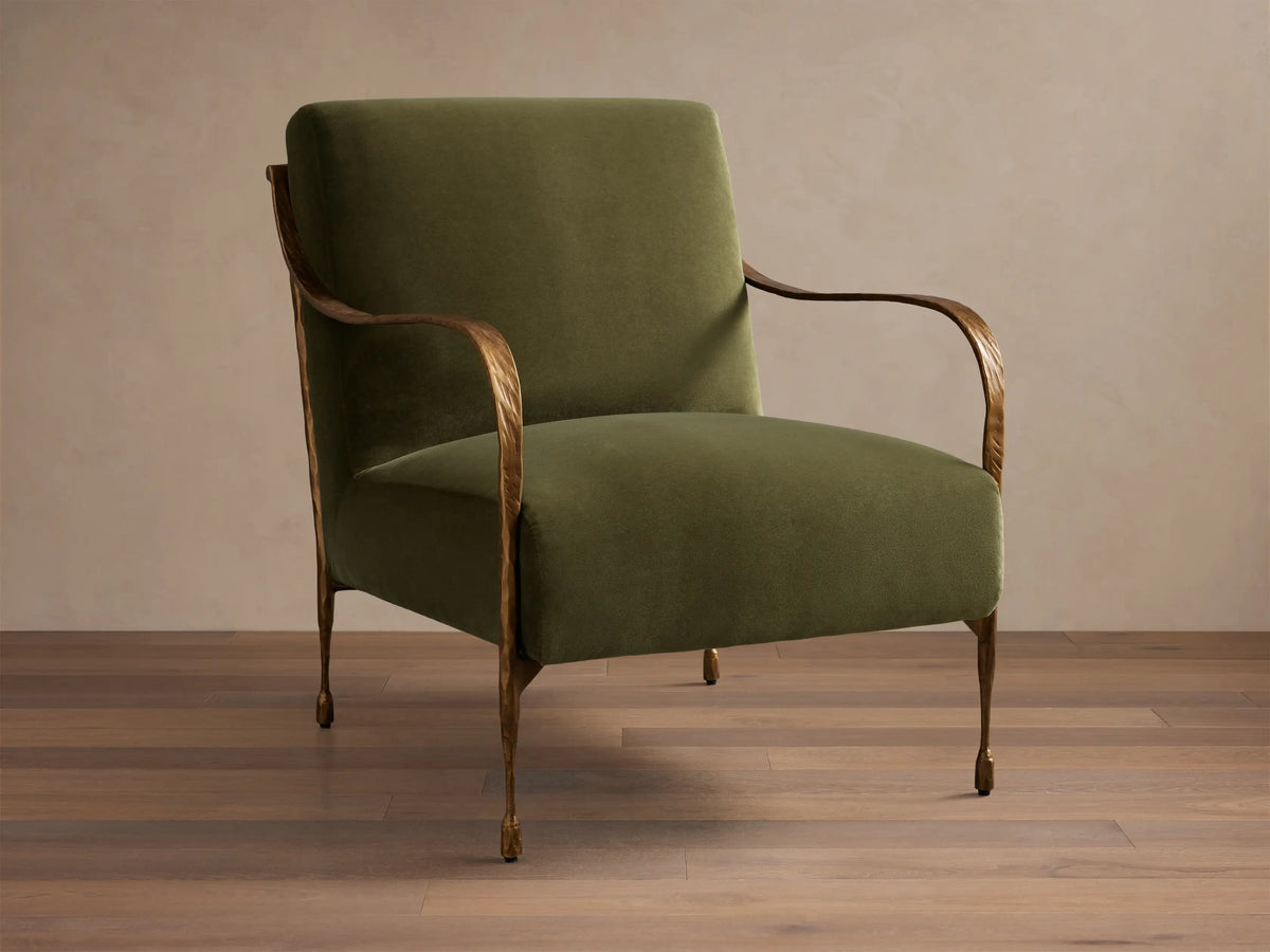 Front view of an olive green upholstered Gwen Chair with hand-hammered brass finish on the iron arms and tapered legs.