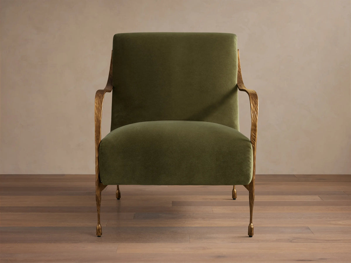 Front view of an olive green upholstered Gwen Chair with hand-hammered brass finish on the iron arms and tapered legs.