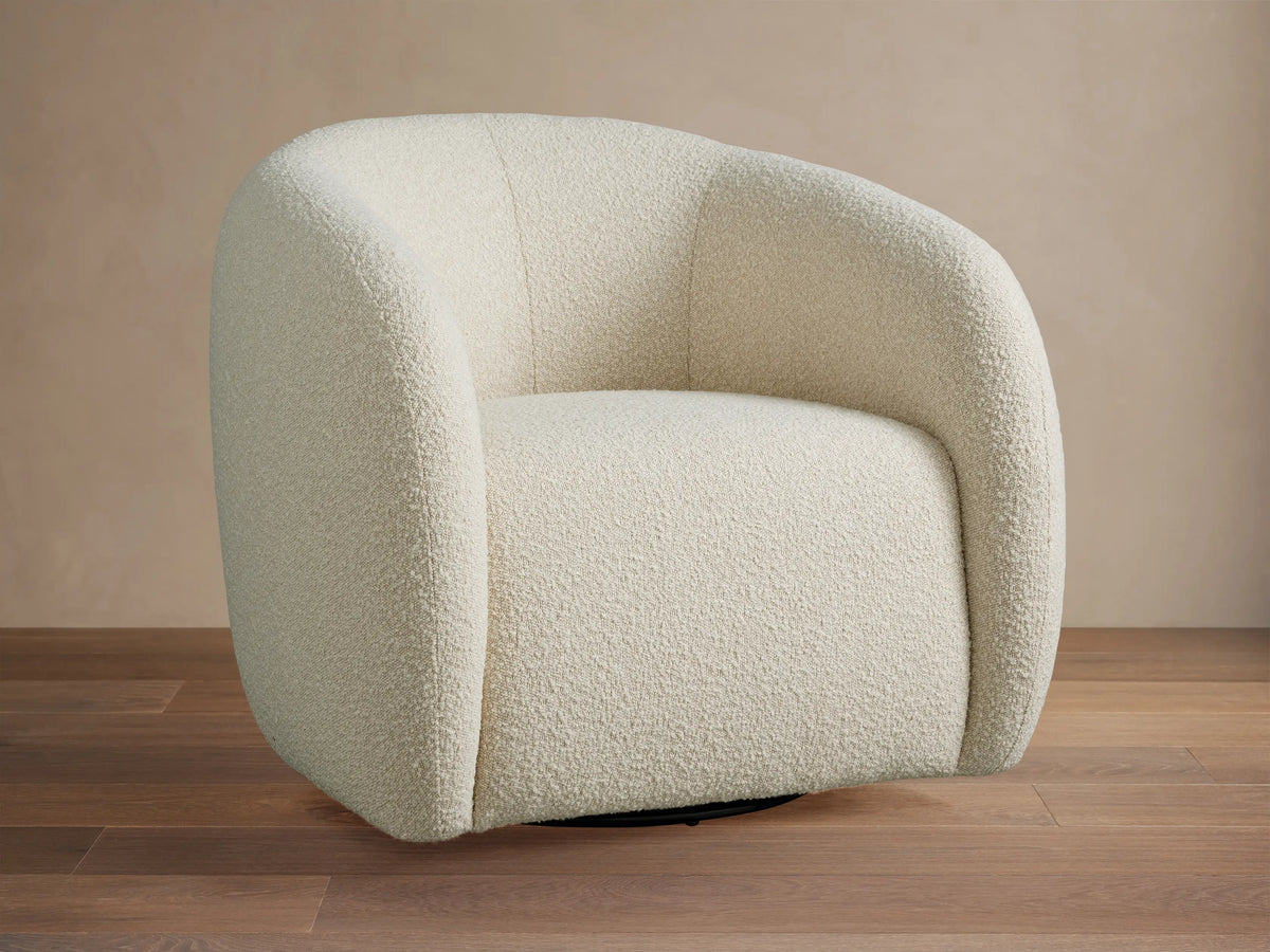 Fresno Swivel Chair, a rounded off-white boucle chair with a black swivel base, angled on a wood floor against a beige wall.