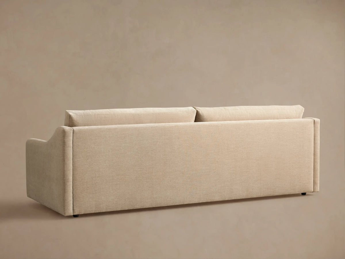 Angled view of Kipton Slope Arm Sofa, highlighting its sloped arm. Cream-colored fabric covers the arm, two seat, and back cushions.
