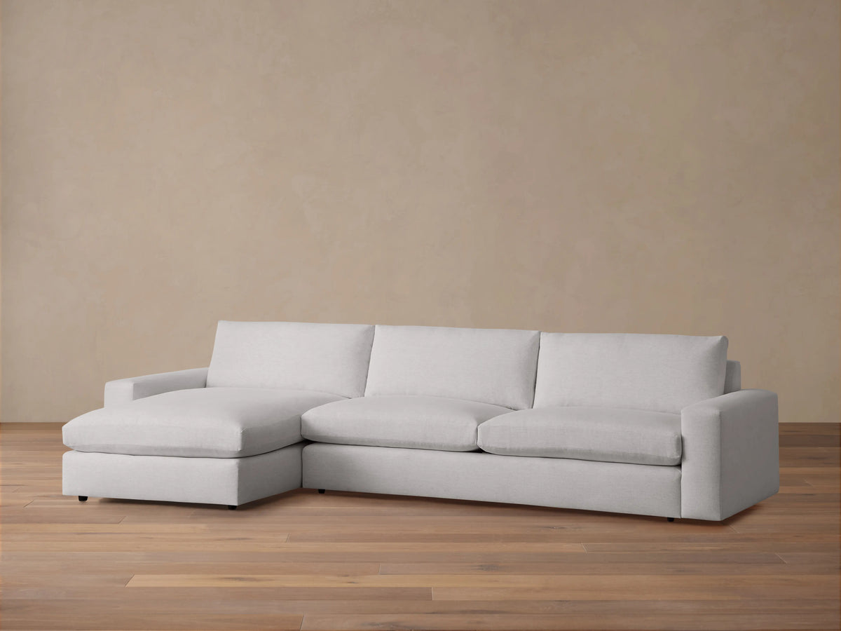 Kipton Wide Arm Two-Piece Chaise Sectional in light gray fabric on wood floor, featuring wide arms, three back cushions, and a chaise on the left.