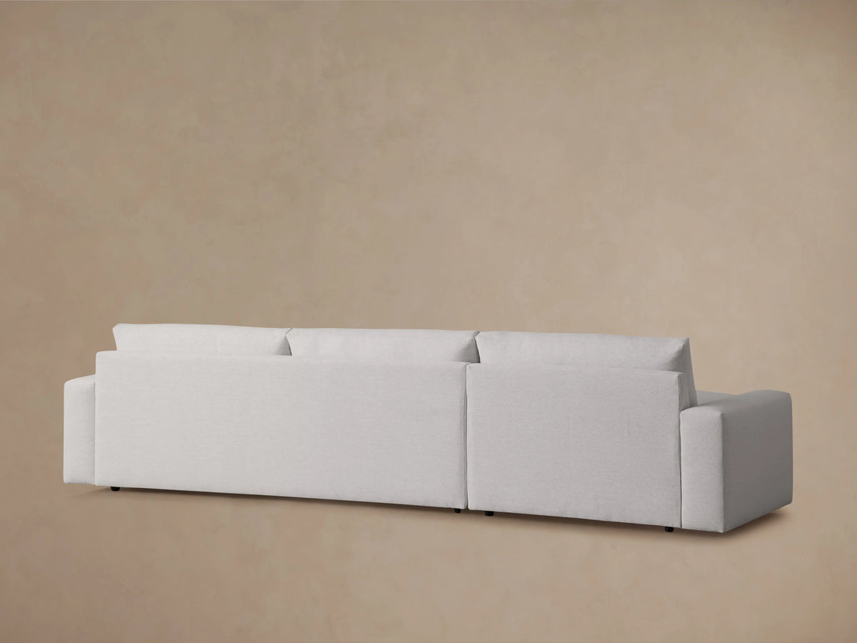 Close-up of the Kipton Wide Arm Two-Piece Chaise Sectional, featuring a light beige fabric, wide armrest, and plush seat cushion.