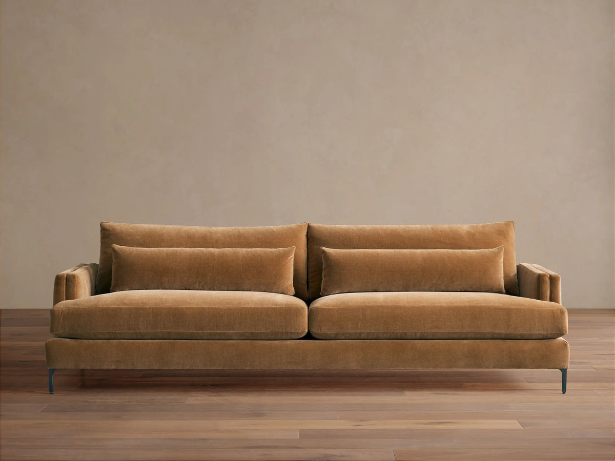 Sumner Sofa: Large, camel-colored velvet sofa with two seat cushions, two back cushions, and two lumbar pillows, on a wood floor.