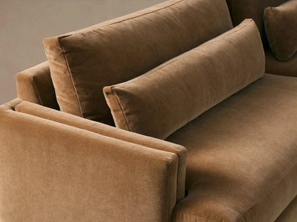 A plush Sumner Sofa in golden brown velvet with two seats, two back cushions, two lumbar pillows, and thin black legs on a wood floor.