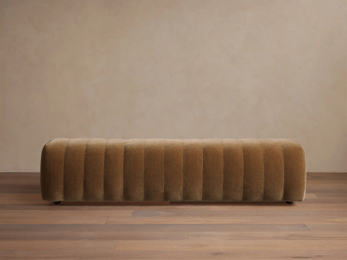 Fresno Channel-Stitched Bench. Long, rectangular, golden-brown upholstered bench with vertical channels, on a wooden floor.