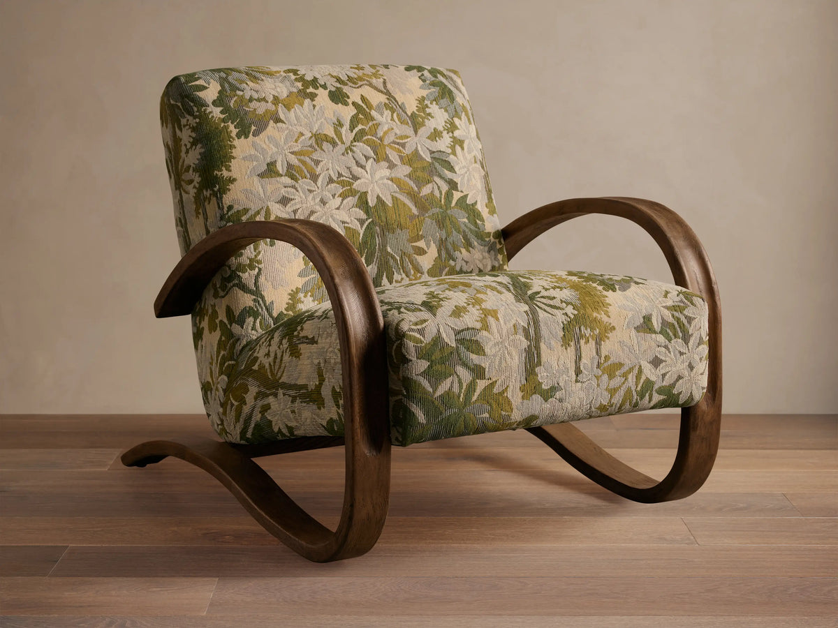 Allora Chair with a distinctive curved mocha wood frame & green, cream, and beige floral patterned upholstery on a wooden floor.
