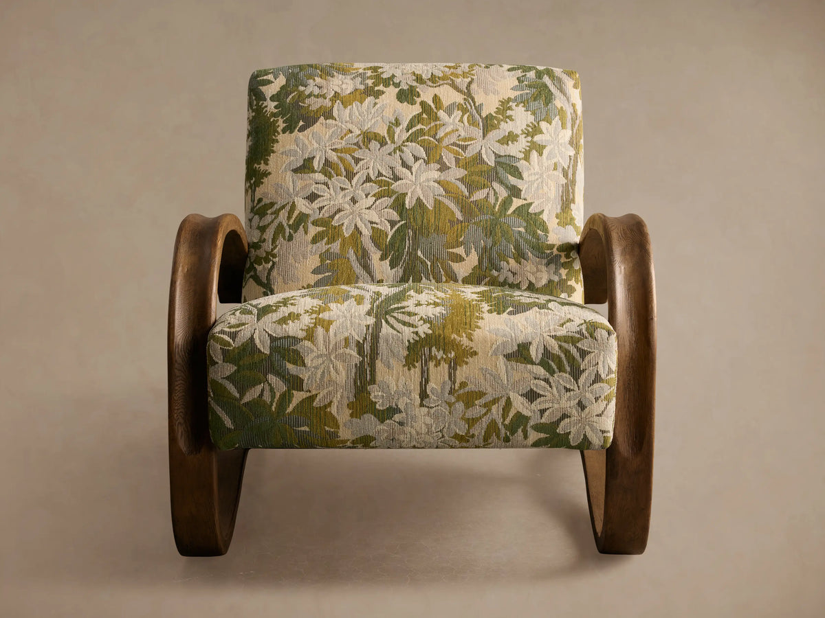 Allora Chair with a distinctive curved mocha wood frame & green, cream, and beige floral patterned upholstery on a wooden floor.