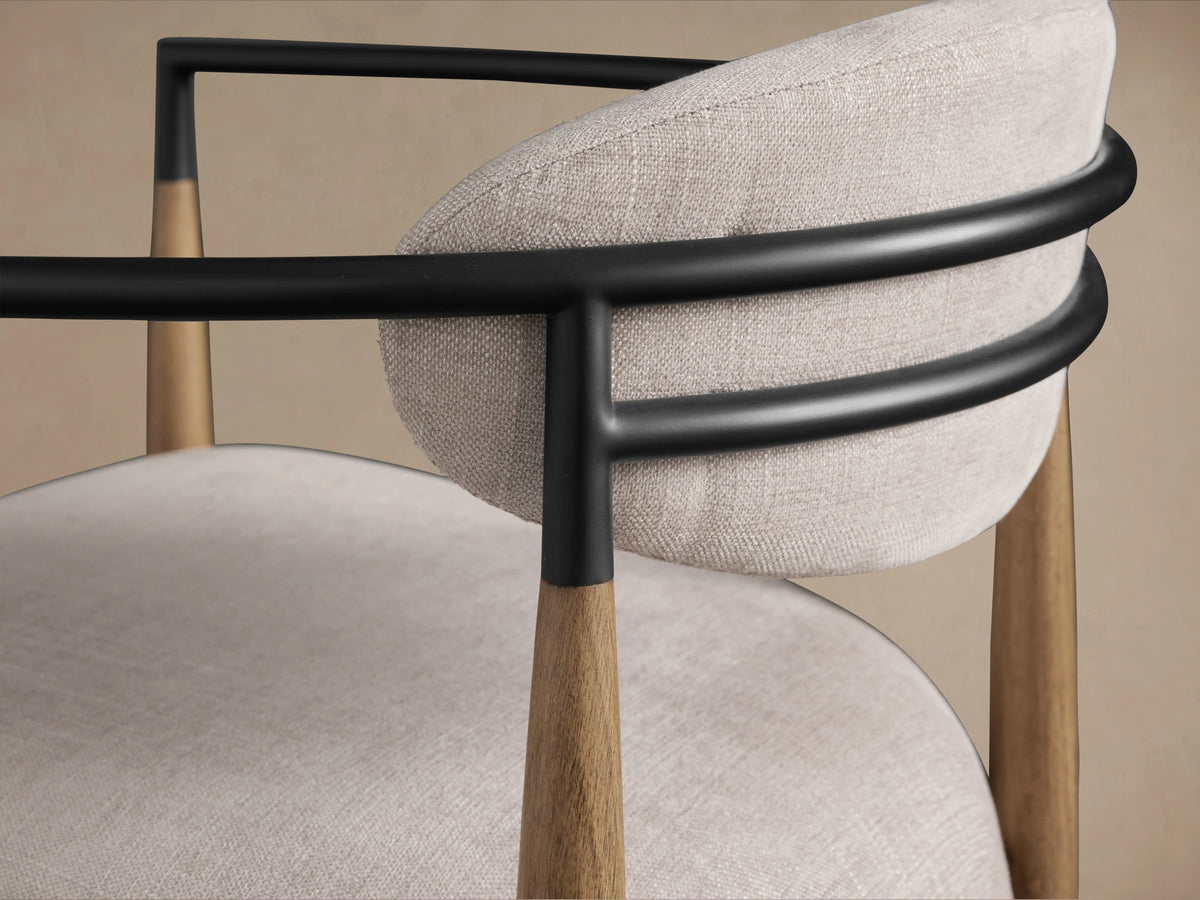 Jagger Chair in Natural with light fabric seat and backrest, wooden frame, and curved dark armrests on a wooden floor.