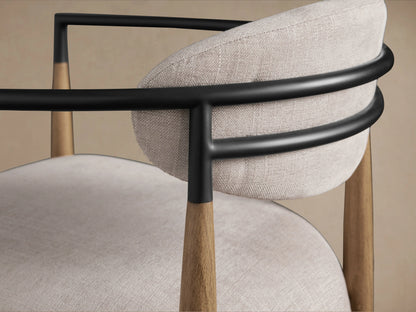 Jagger Chair in Natural with light fabric seat and backrest, wooden frame, and curved dark armrests on a wooden floor.