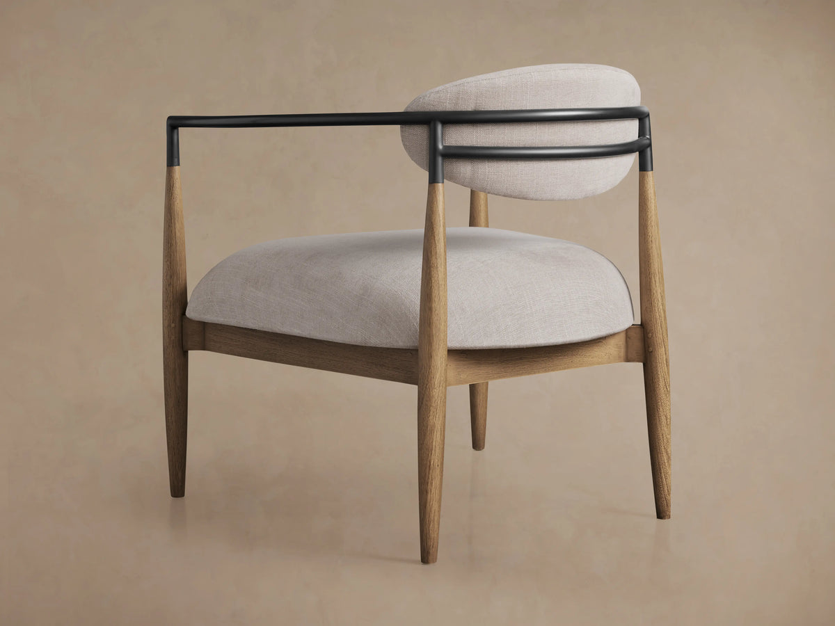 Jagger Chair in Natural featuring a cushioned seat and backrest in light fabric, with a black metal frame and wooden legs.