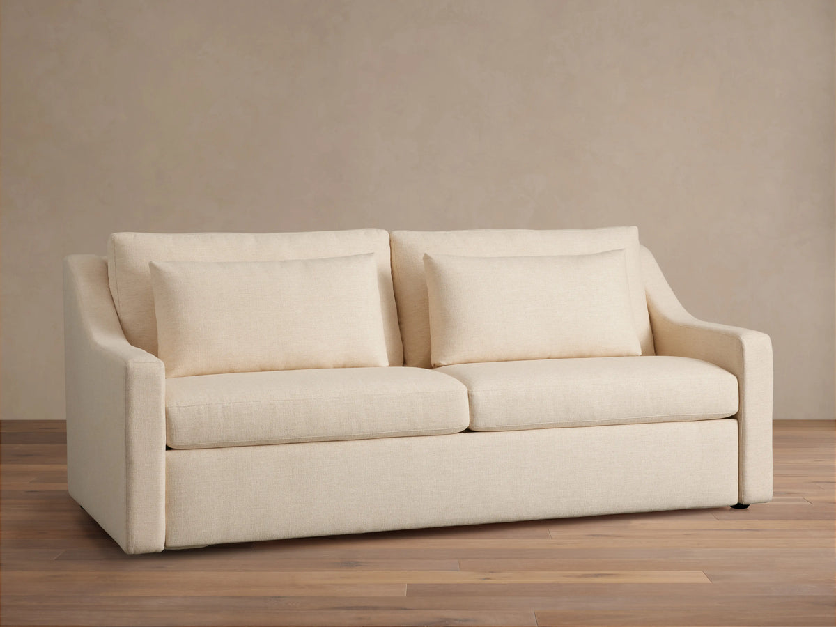 Ashby Luxury Sleeper Sofa in a light cream fabric, featuring plush cushions and clean lines, set against a neutral background.