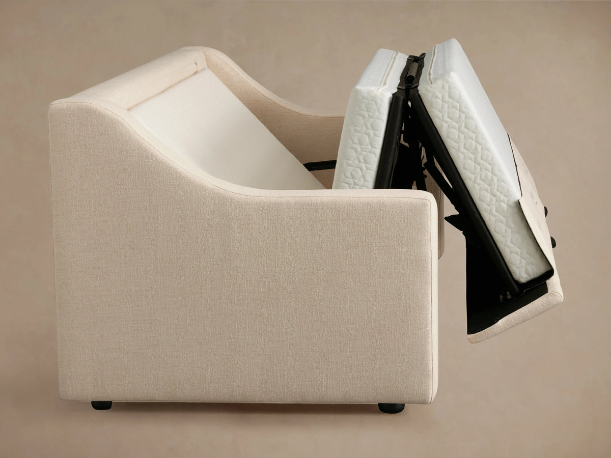 Ashby Luxury Sleeper Sofa, open to reveal a light-colored mattress with textured pattern. Sofa armrests visible, upholstered in matching fabric.