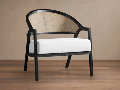 Aimee Chair: black oak frame, curved rattan cane back, and white Nomad Snow upholstered seat on a wood floor.