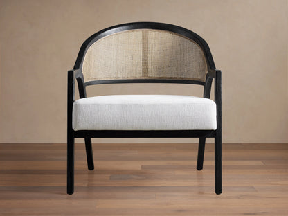 Aimee Chair: black oak frame, curved rattan cane back, and white Nomad Snow upholstered seat on a wood floor.