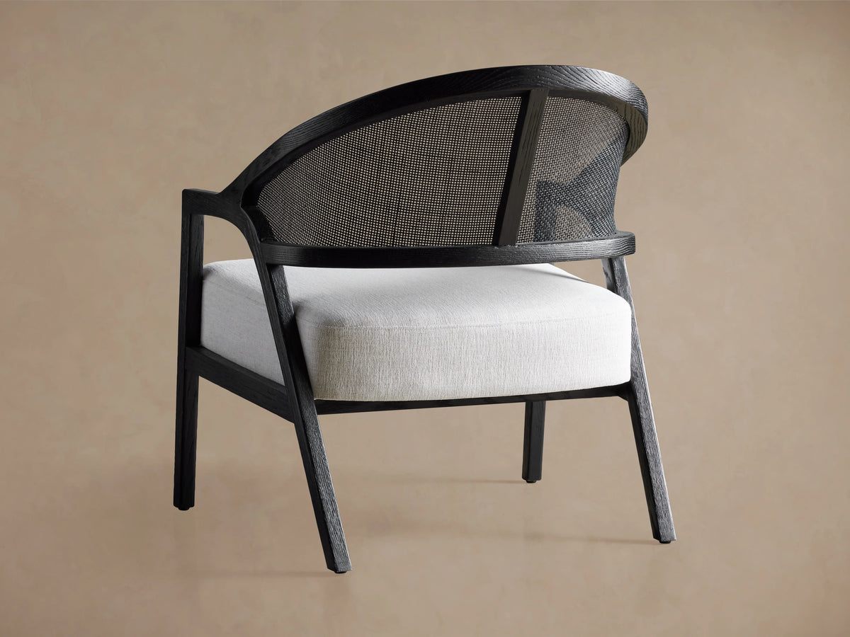 Close-up of Aimee Chair: dark oak frame with curved rattan back, and white Nomad Snow upholstered seat cushion.