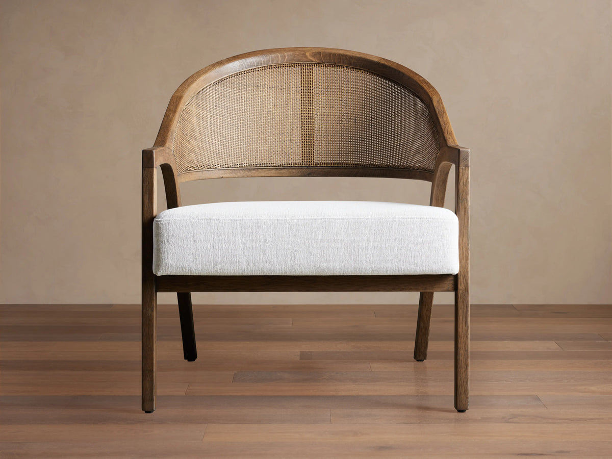 Aimee Chair: dark oak wood frame with curved rattan back and white Nomad Snow upholstered seat, on a wood floor.