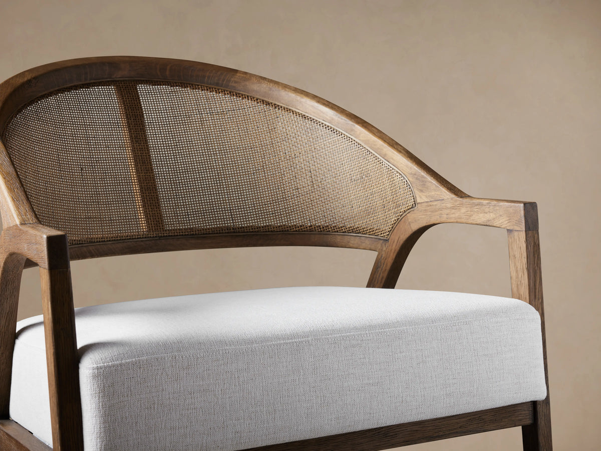 Aimee Chair: dark oak frame, arched rattan cane back, and thick white Nomad Snow upholstered seat, front view on wood floor.