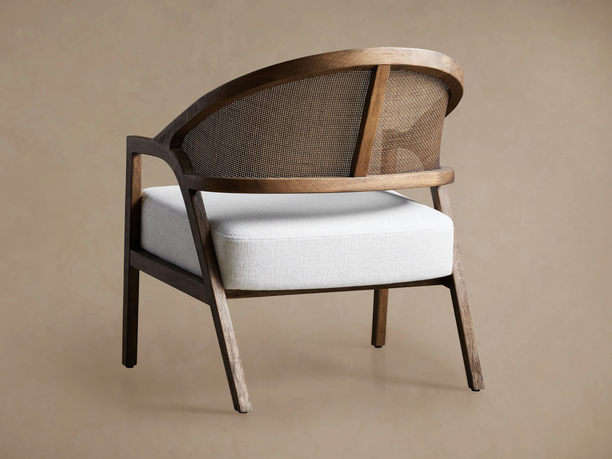 Close-up of Aimee Chair in Nomad Snow, showing light gray fabric seat, curved oak frame, and natural rattan cane back.