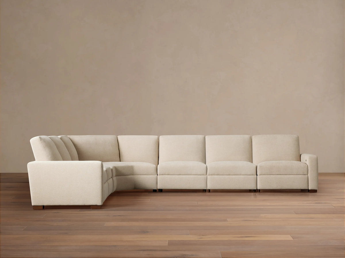 Remington Six-Piece Motion Sectional, light beige fabric, L-shaped, shown on a wooden floor against a warm beige wall.