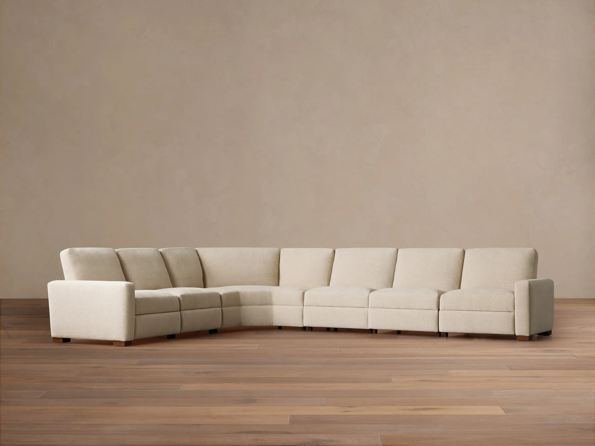 Remington Six-Piece Motion Sectional, light beige fabric, L-shaped, shown on a wooden floor against a warm beige wall.