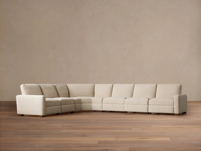 Remington Six-Piece Motion Sectional, light beige fabric, L-shaped, shown on a wooden floor against a warm beige wall.