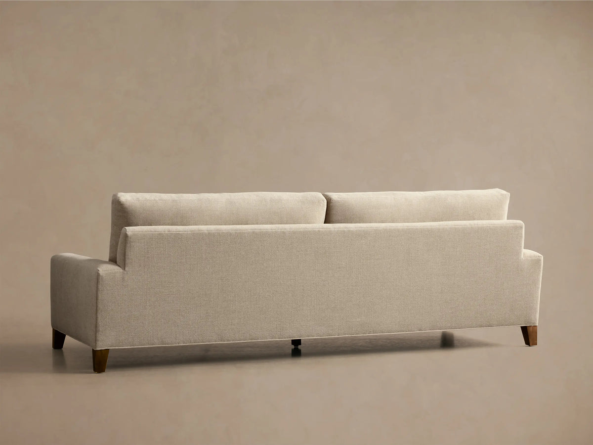 Front and side view of a light beige Remington Elevated Sofa with channel-stitched seat cushions, square arm, and mocha finish feet.