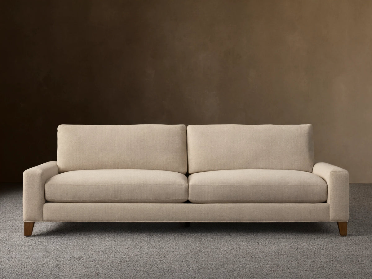 Front view of the light beige Remington Elevated Sofa with two seat cushions, two back cushions, and dark mocha-finished elevated legs.