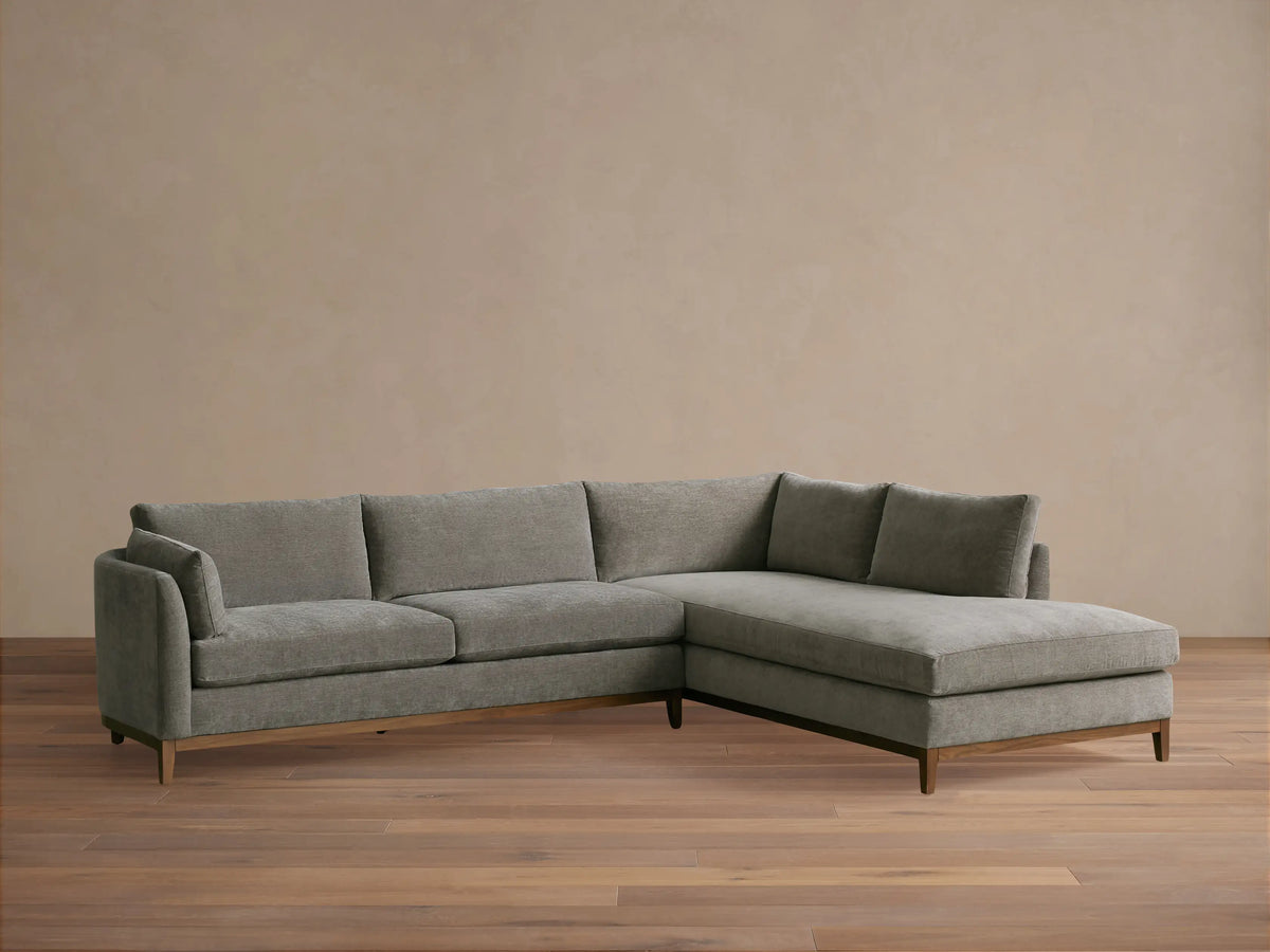Bainbridge Two-Piece Bumper Sectional, grey fabric with wooden base, L-shaped, right-hand facing chaise, on wood floor.