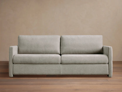 Reece Sleeper Sofa in light gray fabric, modern two-seater design with square arms, on a wooden floor against a tan wall.