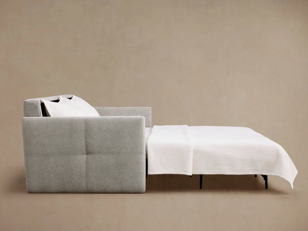 Light grey Reece Sleeper Sofa partially unfolded. Left shows side of sofa with stitched channels; right reveals extended bed with white mattress.