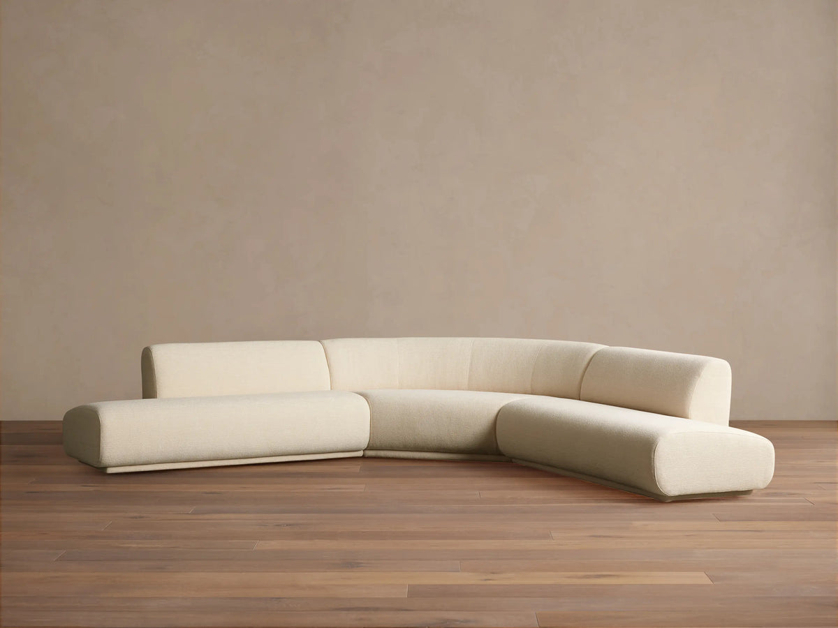 Cream Gianni Three-Piece Curved Bumper Sectional on a wooden floor against a tan wall, showing its elegant, modern design.