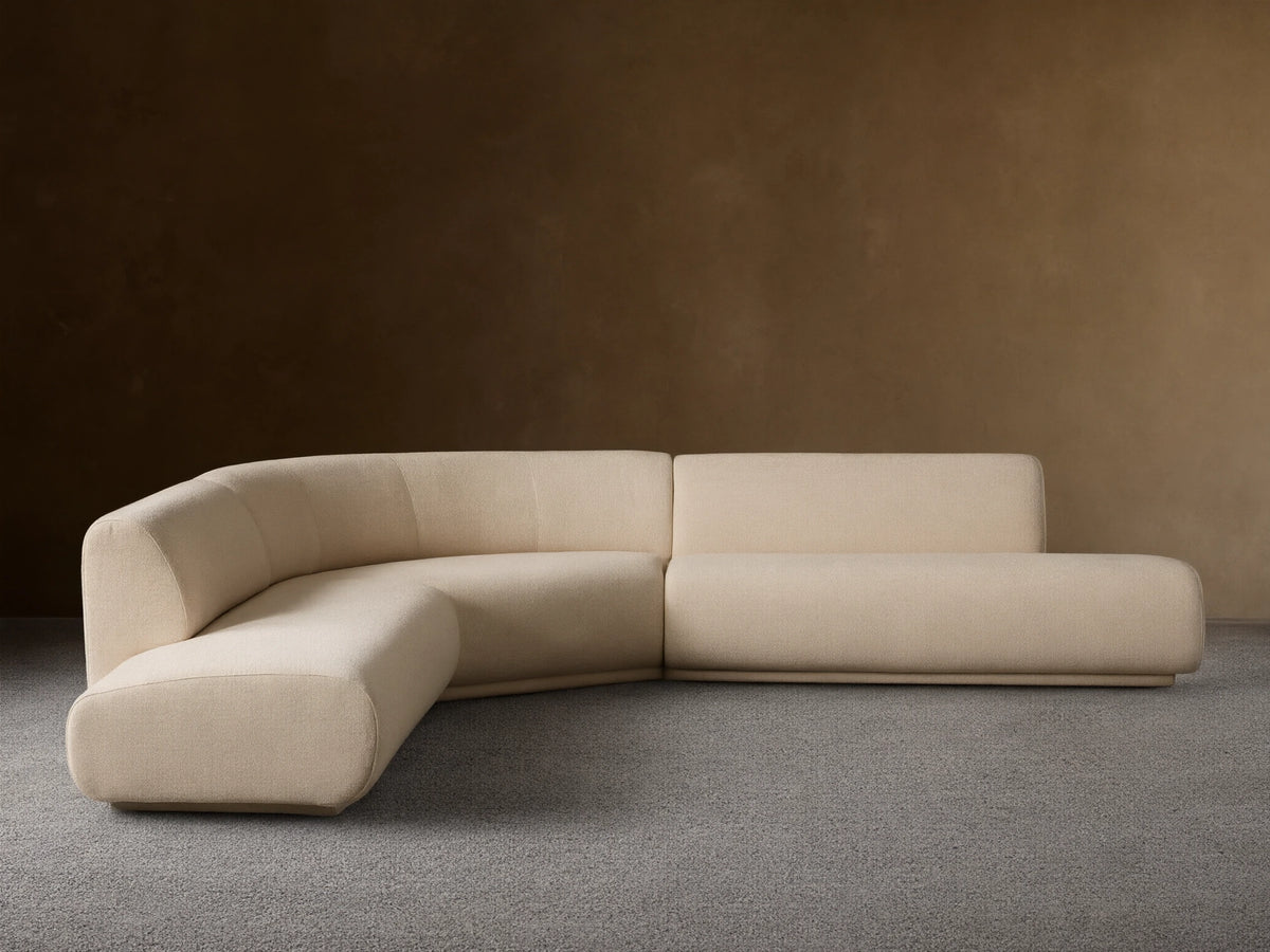 Cream Gianni Three-Piece Curved Bumper Sectional on a wooden floor against a tan wall, showing its elegant, modern design.