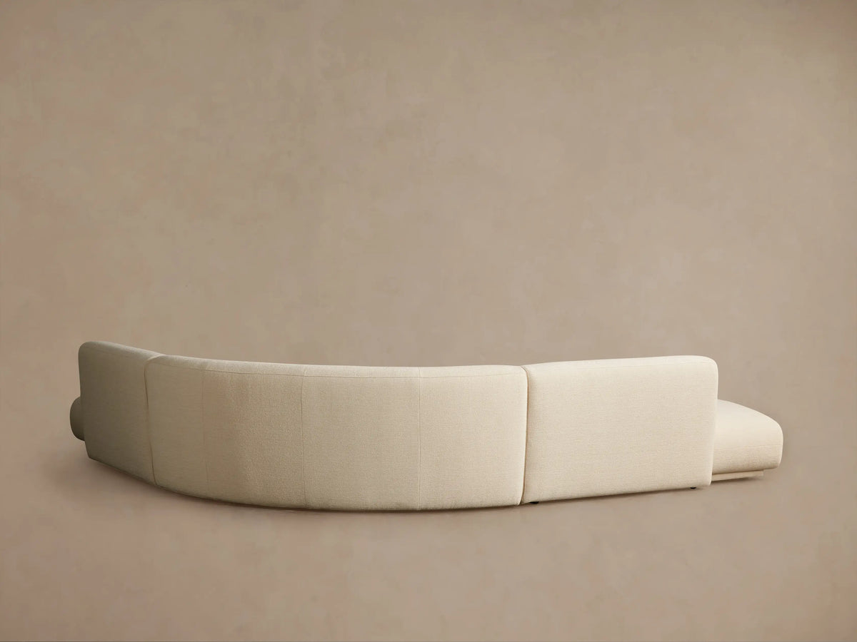 Close-up of a Gianni Three-Piece Curved Bumper Sectional, light beige textured fabric with a prominent curve, viewed from above right.