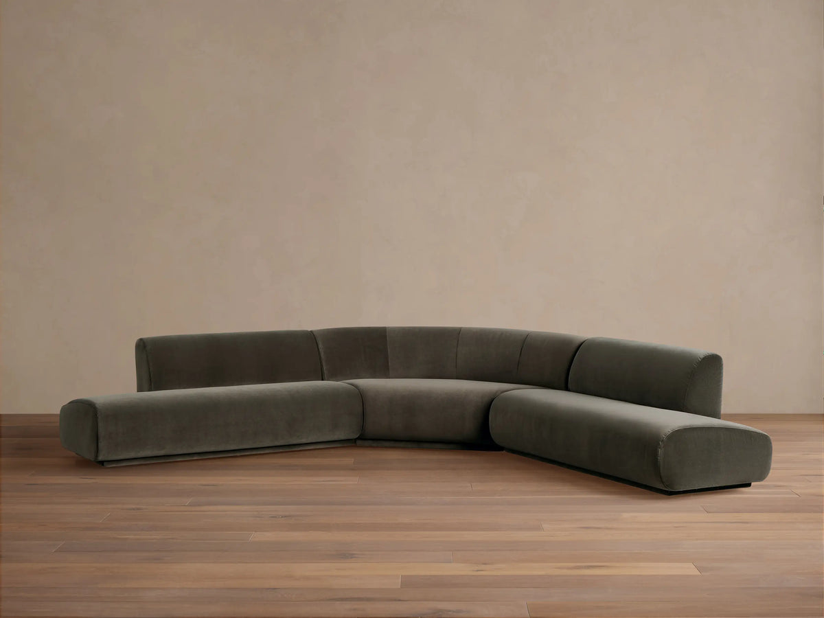 Gianni Three-Piece Curved Bumper Sectional in dark gray-green fabric, angled on a wood floor against a neutral wall.