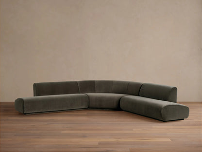 Gianni Three-Piece Curved Bumper Sectional in dark gray-green fabric, angled on a wood floor against a neutral wall.